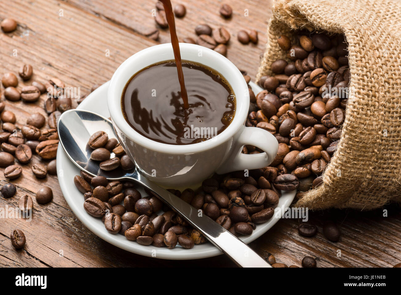 Füllen Sie eine Tasse Kaffee auf Holztisch, mit Leinensack und Kaffeebohnen. Stockfoto