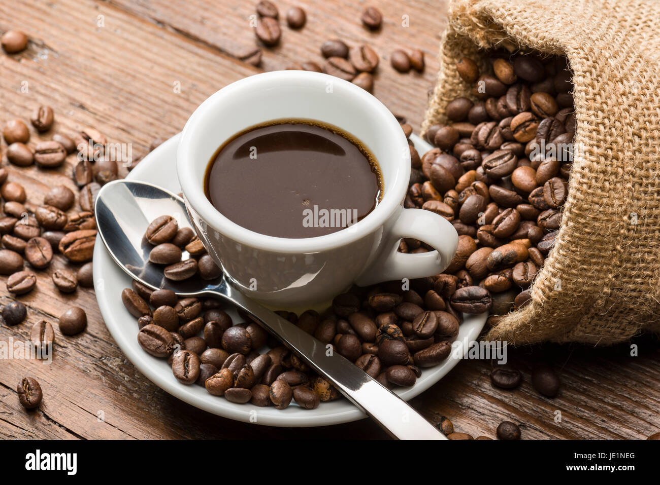 Tasse Kaffee mit Leinensack und Kaffeebohnen auf Holztisch. Stockfoto