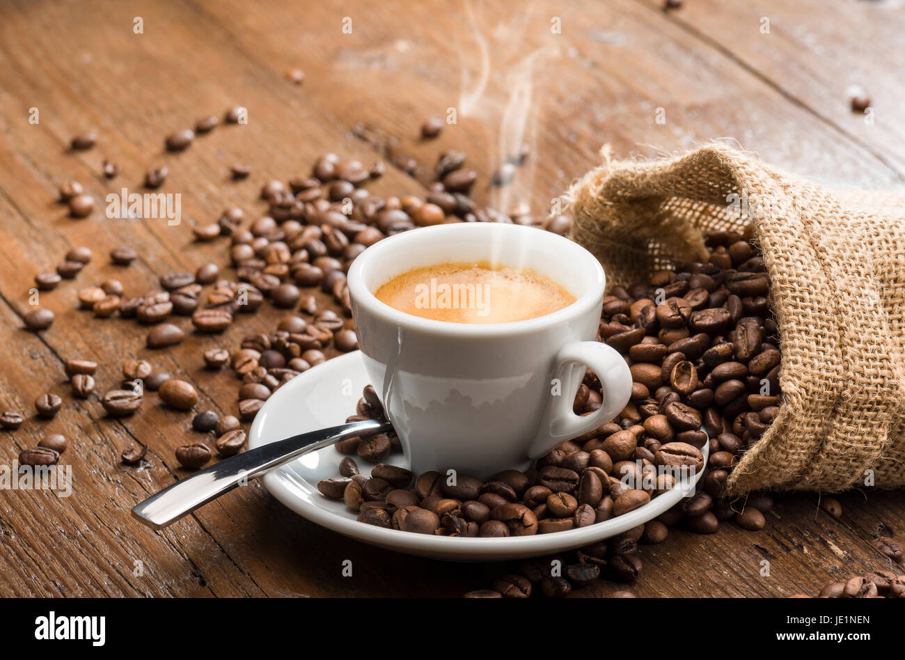 dampfende Tasse Kaffee mit Leinensack und Kaffeebohnen auf Holztisch. Stockfoto