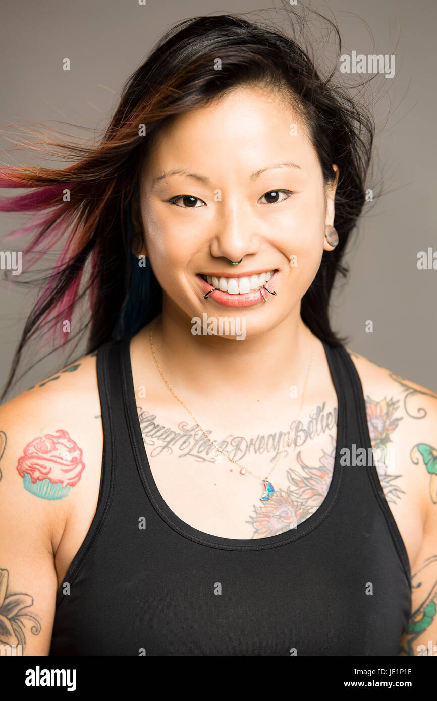 Junge Asiatin mit gefärbtes Haar und Tattoos und Piercings lächelt viewer Stockfoto