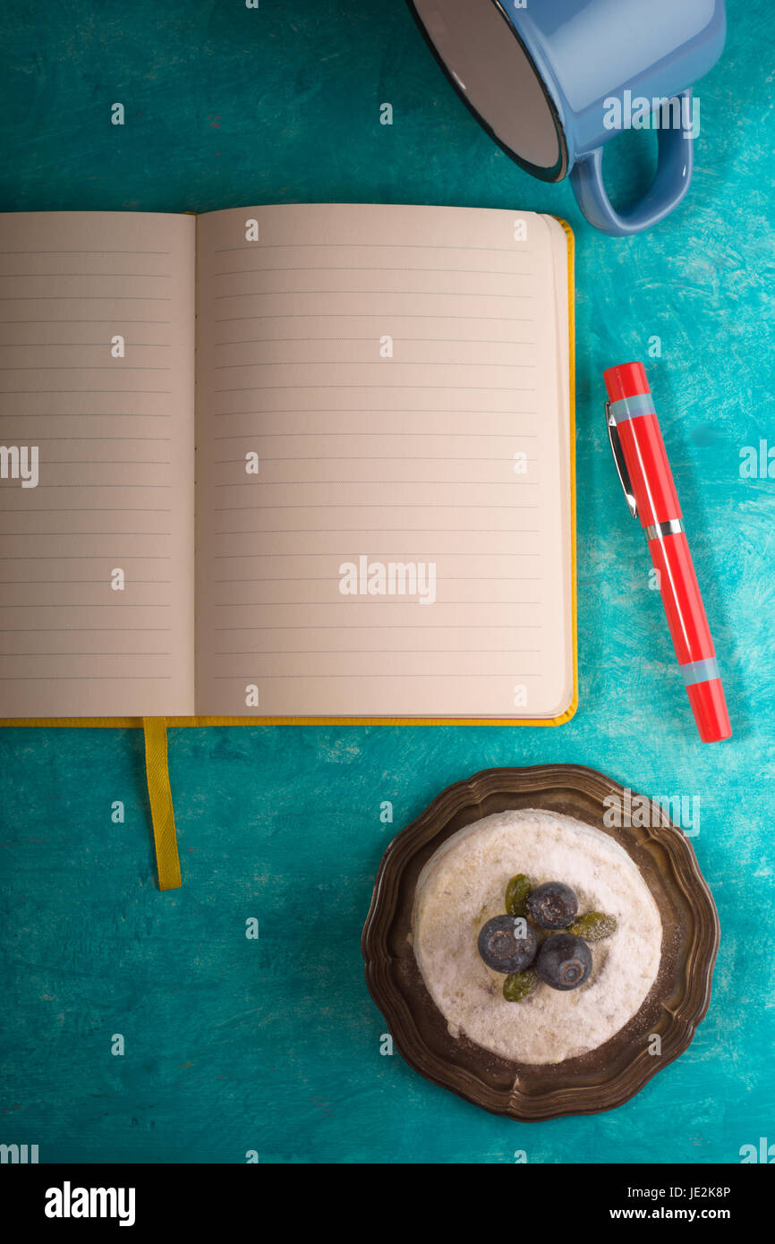 Kuchen, Tasse, Notizbuch, Serviette und Stift auf dem blaugrünen Hintergrund vertikale Stockfoto