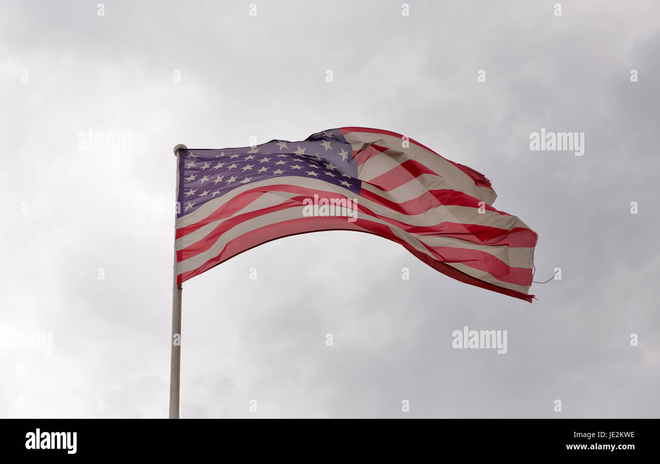 Verblasst und zerfetzt amerikanische Flagge winken gegen ein bewölkter Himmel Stockfoto