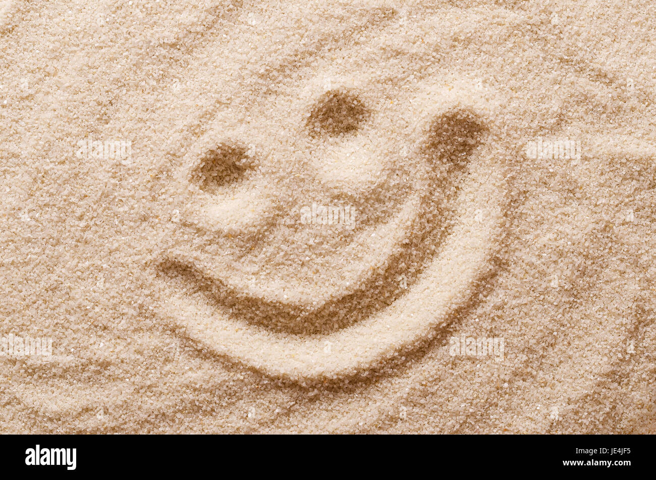 Happy lächelndes Gesicht im Sand. Augen und Mund mit einem Finger in trockenen Trinkwasserbehältern Sand gezeichnet. Makrofoto Nahaufnahme von oben. Stockfoto