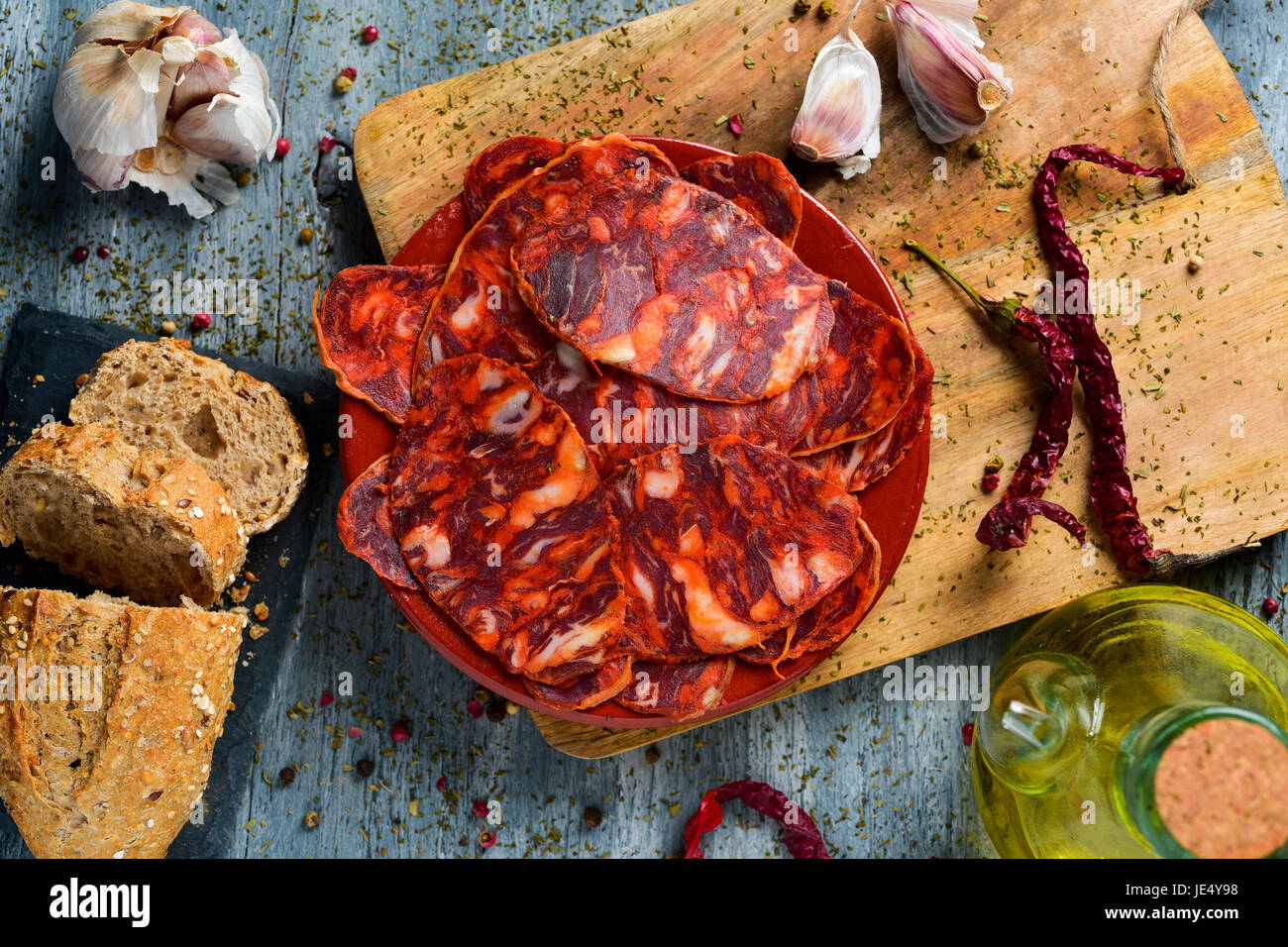 High-Angle Shot eines Steingut Platte mit einige Scheiben der spanischen Chorizo, Wurstwaren Wurst, einige Scheiben Brot, ein Glas Menage mit Olivenöl ein Stockfoto