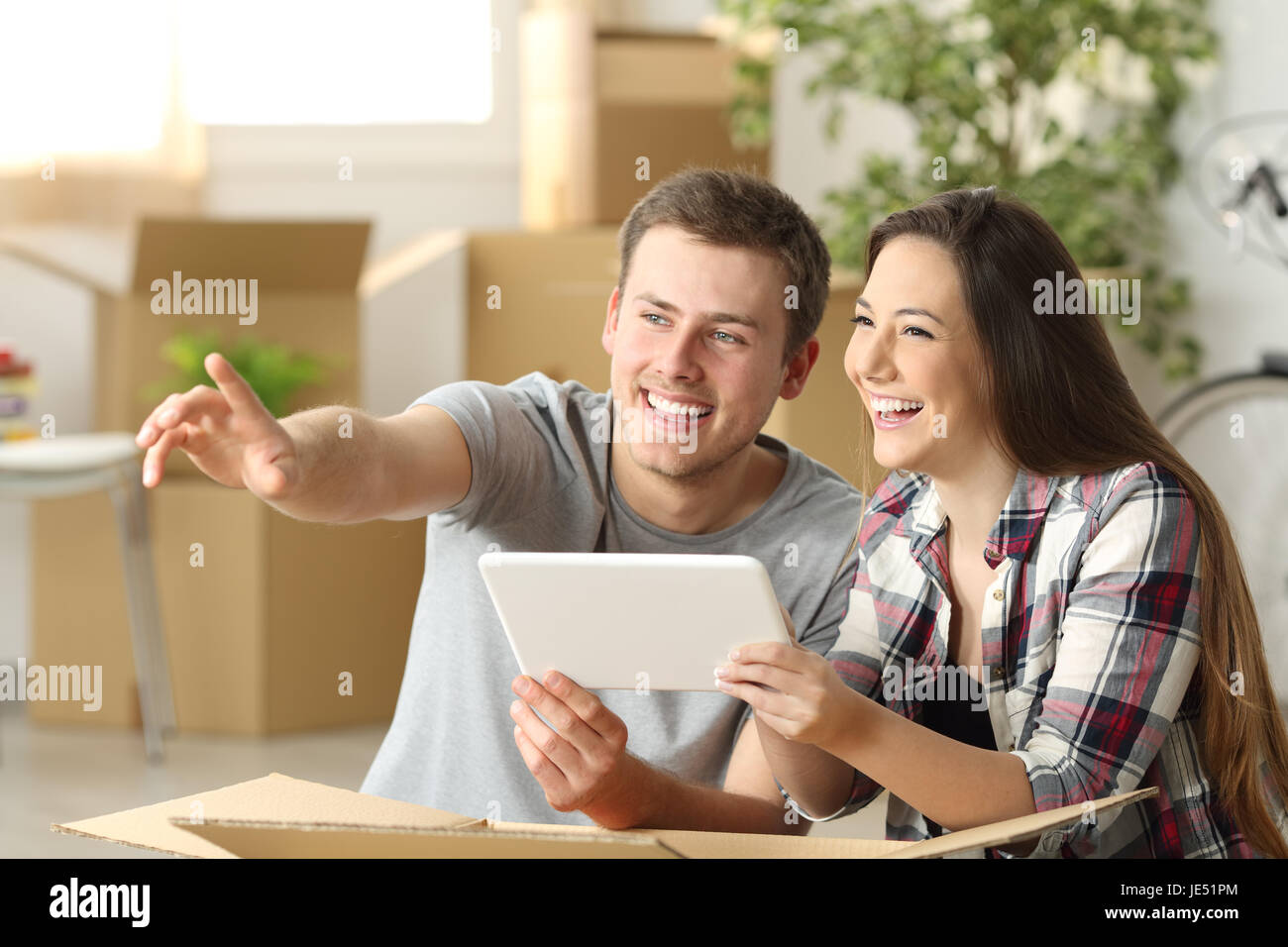 Glückliches Paar zusammen Hausplanung auf Linie mit einer Tablette, die sitzen auf dem Boden zu Hause mit Boxen in den Hintergrund verschieben Stockfoto