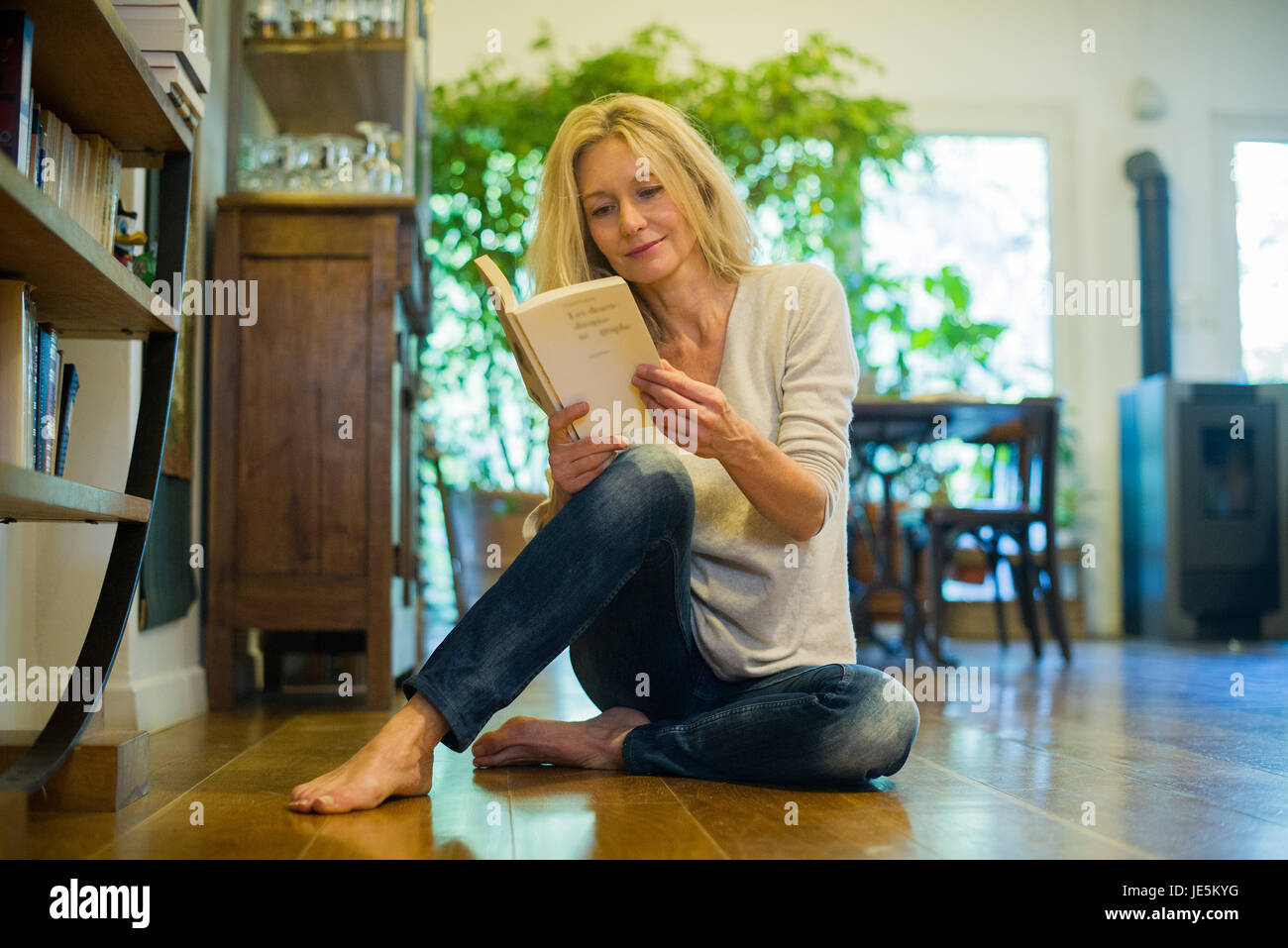 Reife Frau entspannende Erdgeschoss mit Buch zu Hause Stockfoto