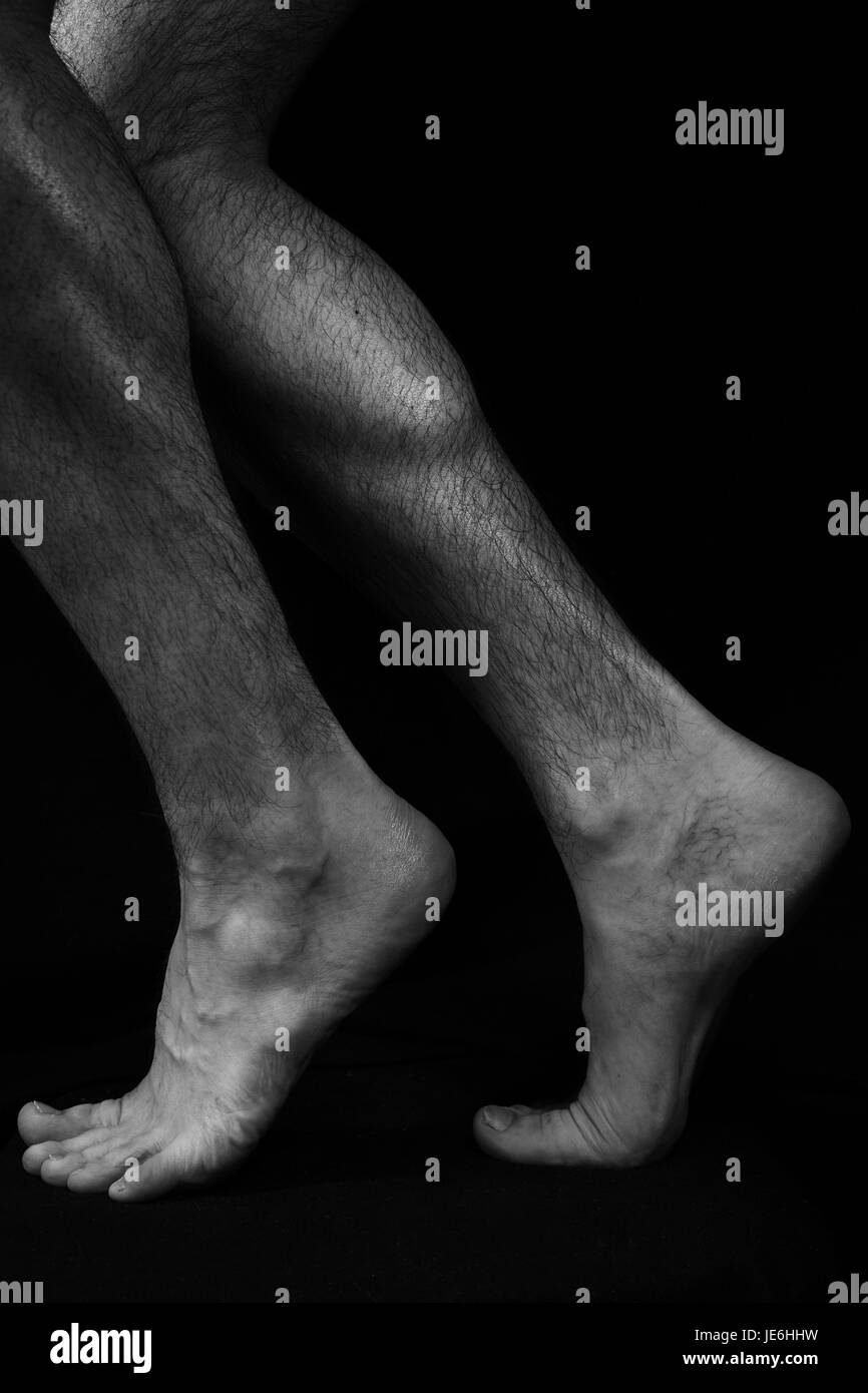 Schön, muskulös, Nackte männliche Füße auf einem schwarzen Hintergrund. Klassische kontrastreiche Kunstfoto Stockfoto