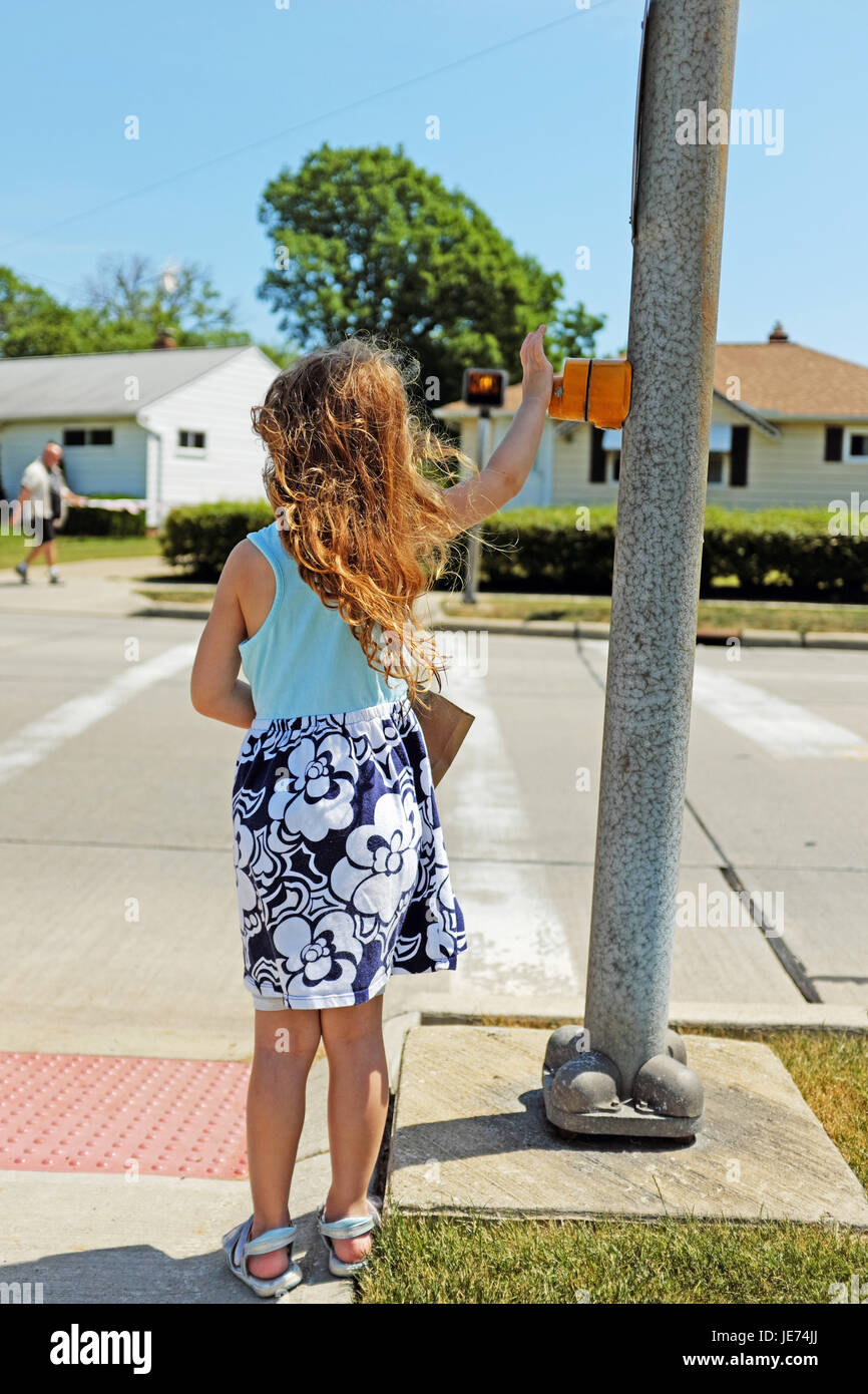 Fünf Jahre altes Mädchen den Zebrastreifen-Knopf drückt, wie ein Mann auf der anderen Seite der Straße in Willowick, Ohio geht. Stockfoto