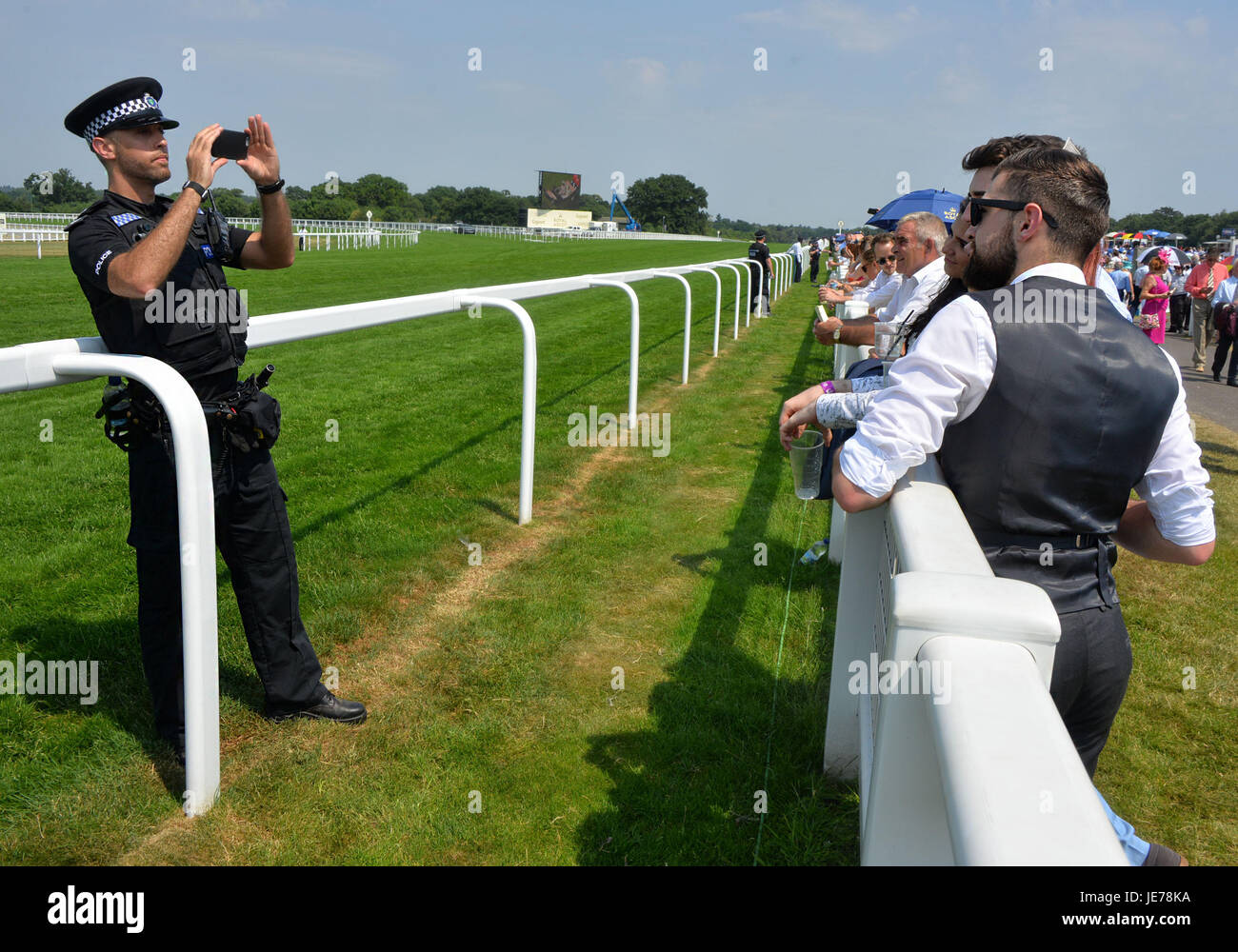 Ein Polizist nimmt Fotos von jungen Männern durch die Rennstrecke am Royal Ascot 2017. Stockfoto