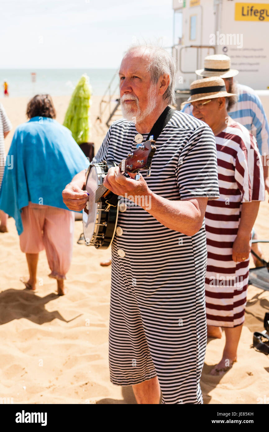 Älterer Mann, 60 Jahre, mit kurzen weißen Brot, tragen Viktorianische Badeanzug, stehend auf Strand Festlegung der Banjo. Stockfoto