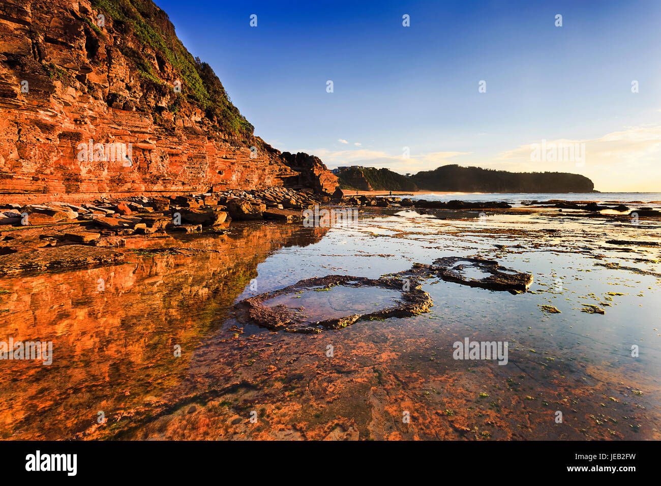 Erwärmen von steigenden Morgen Sune Rock Cliff Landzunge von Narrabeen Strand vor australischen Pazifikküste beleuchtet. Bei Ebbe Aemotio flach flache Pfützen Stockfoto