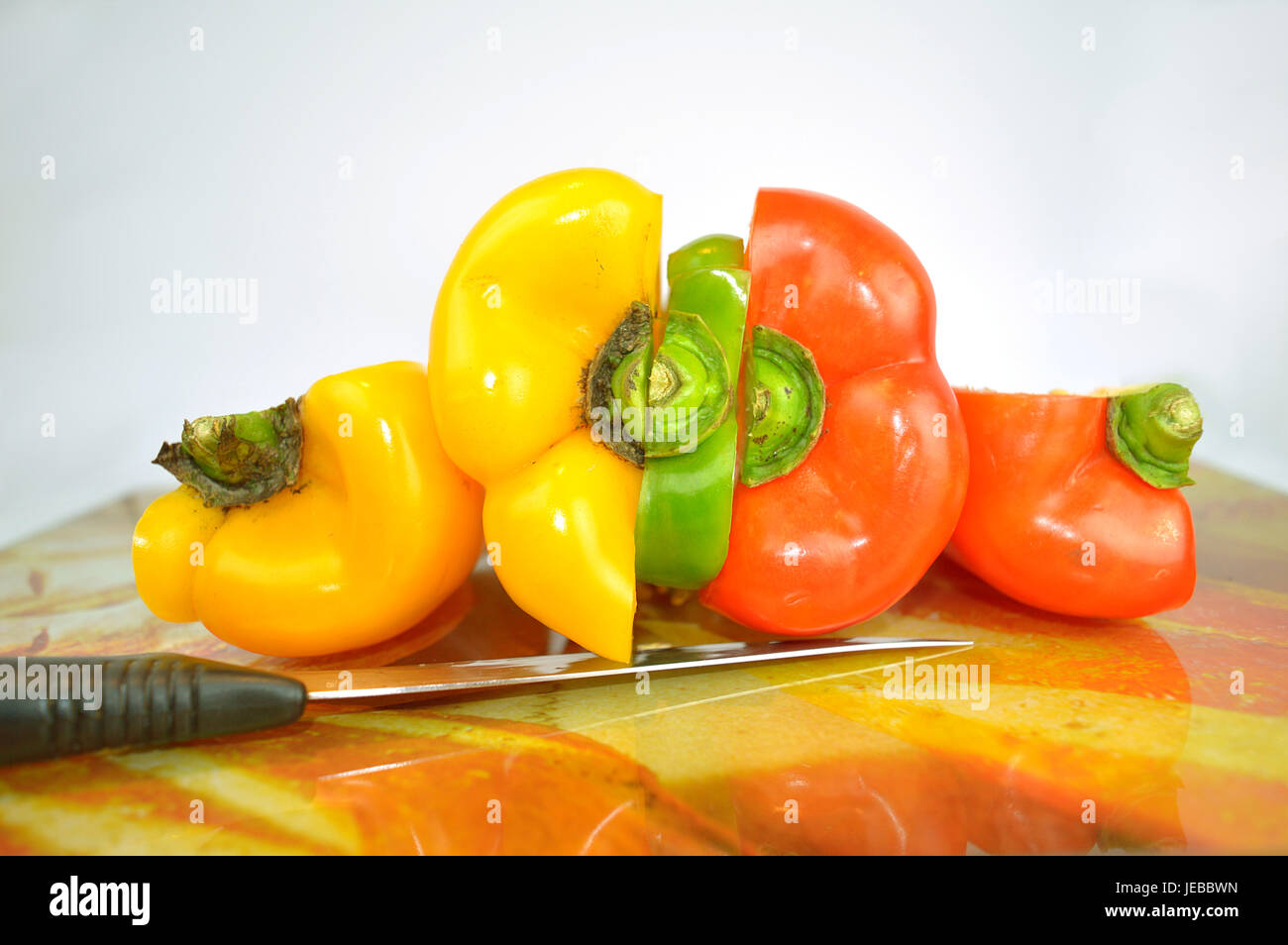 -Gelb, grün und rot - Paprika in Stücke schneiden und zusammen über einen Tisch mit einem Messer Stockfoto