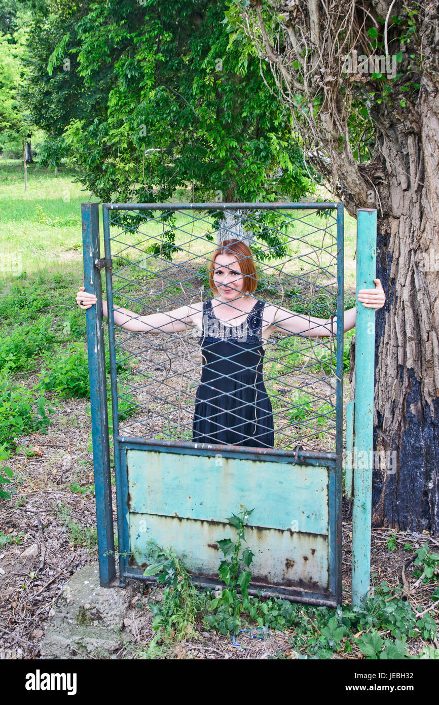 Mädchen posiert hinter einem alten Eisentor. Seit dem Zaun ist einzige Tor erhalten geblieben. Stockfoto