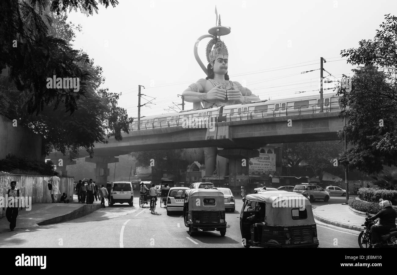 Hindu-Gott Hanuman, überragt von der modernen Metro, Menschen und Verkehr Aufstoßen giftige Dämpfe in Delhi, Indien. Stockfoto