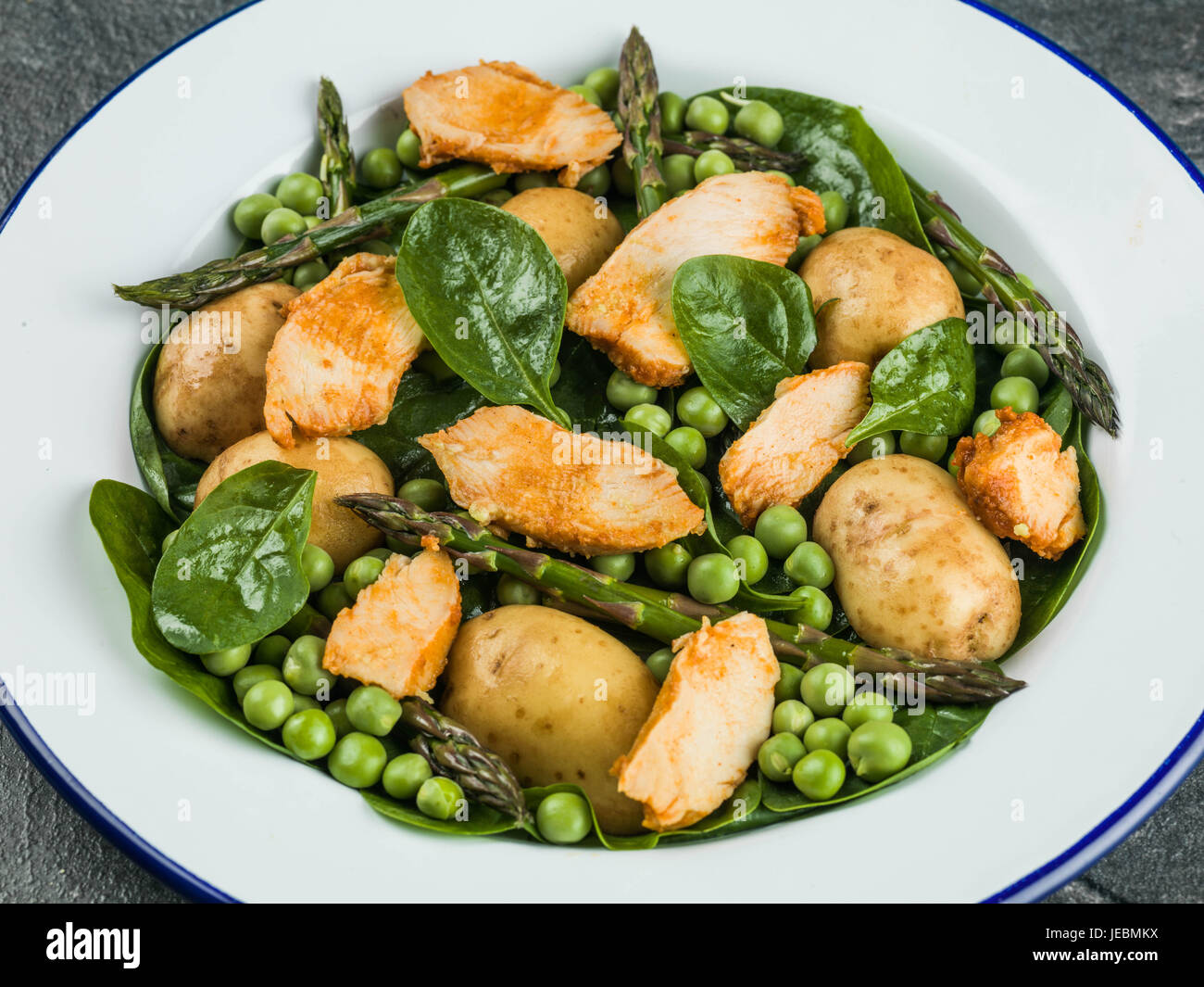 Hähnchen-Salat mit Spargel Erbsen Spinat und Kartoffeln vor schwarzem Hintergrund Stockfoto