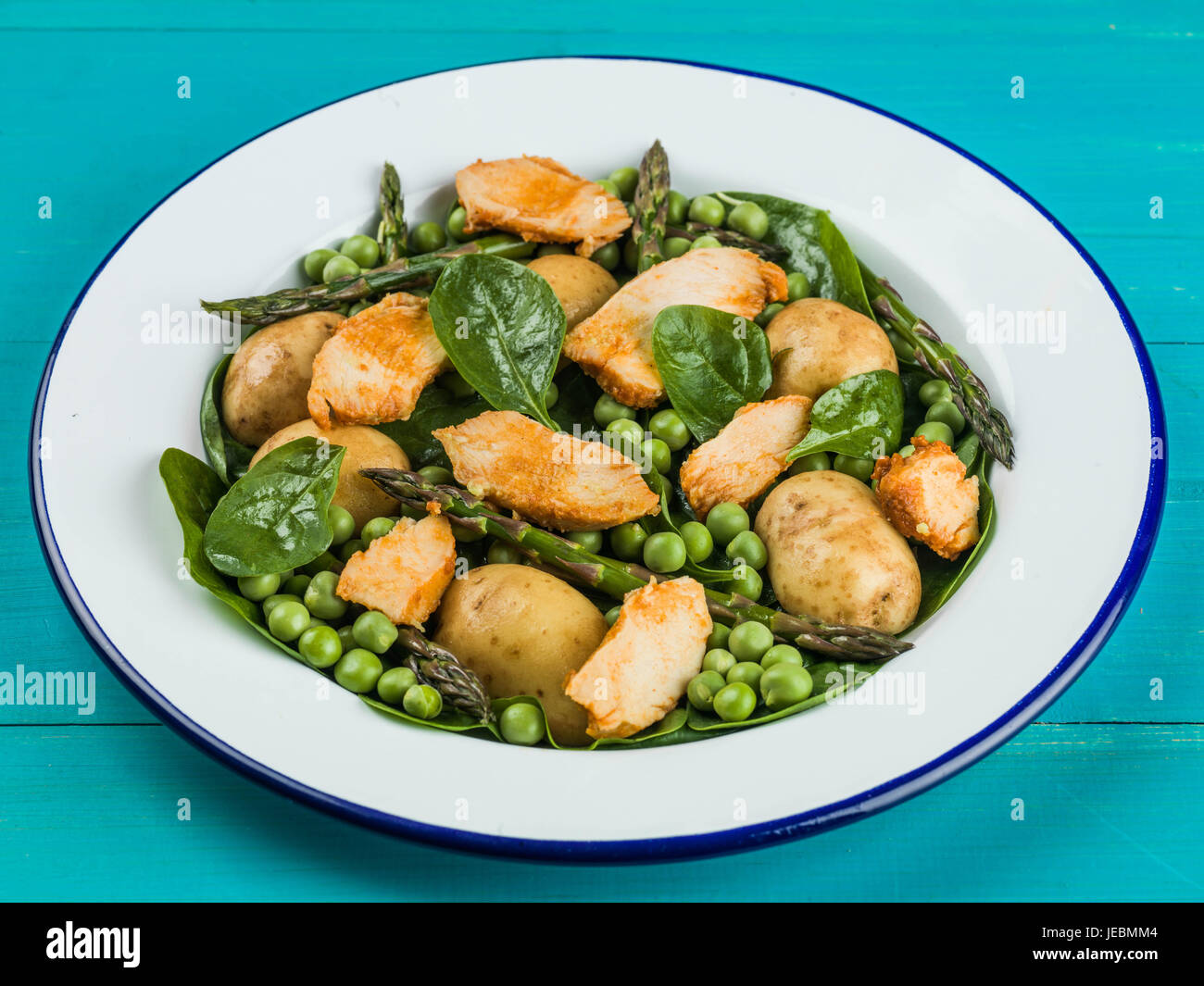 Hähnchen-Salat mit Spargel Erbsen Spinat und Kartoffeln auf blauem Grund Stockfoto
