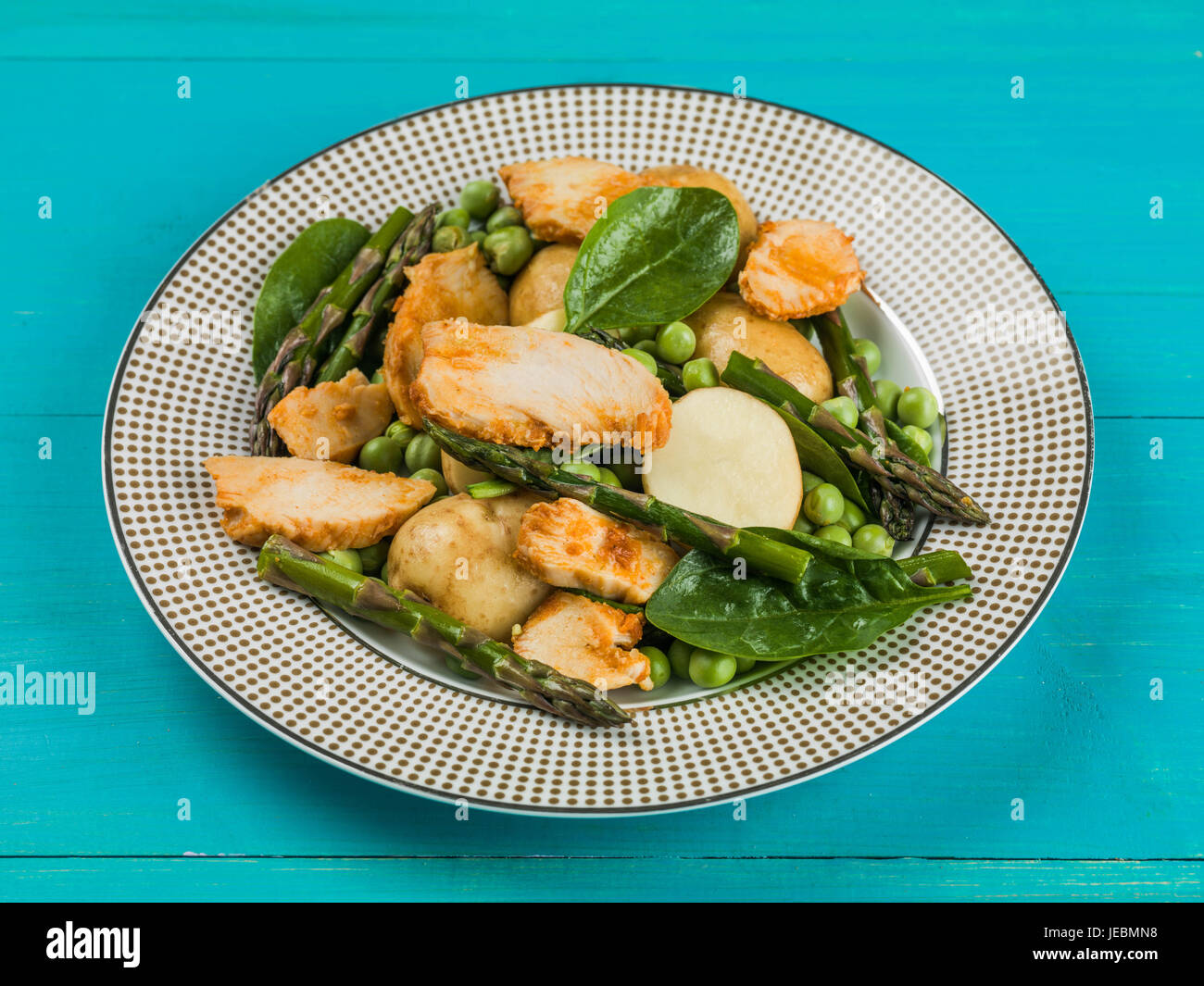Hähnchen-Salat mit Spargel Erbsen Spinat und Salzkartoffeln auf blauem Grund Stockfoto