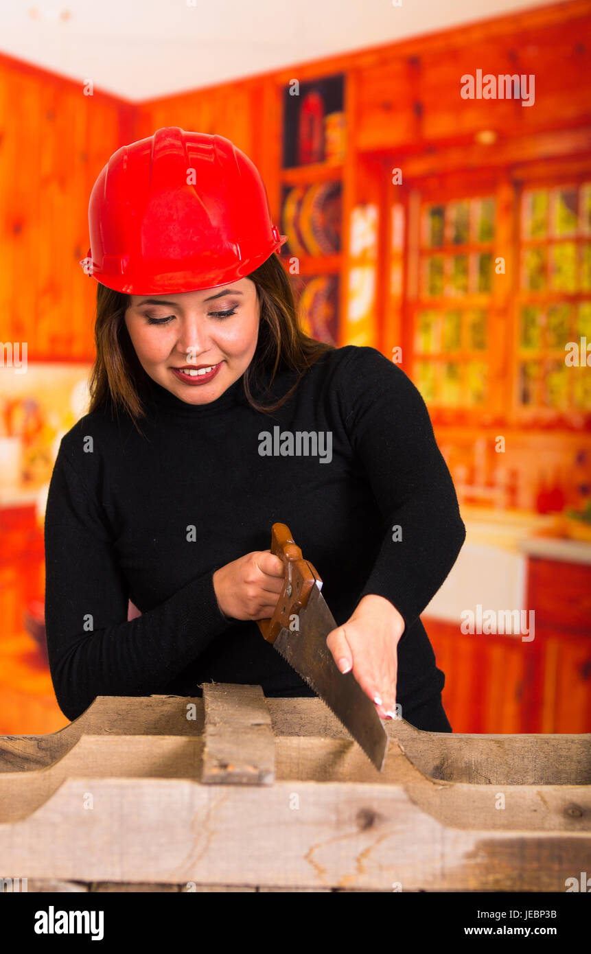 Schöne junge Frau Zimmermann Schneiden von Holz mit einer Säge lächelnd Stockfoto
