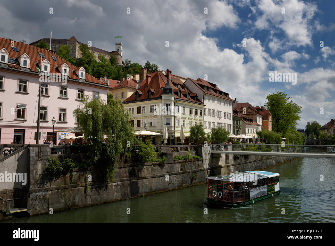 Historische Gebäude am Cankar Quay Ufer des Flusses Ljubljanica an Fisch Brücke mit Ausflugsschiff und Castle Hill von Ljubljana Slowenien Stockfoto