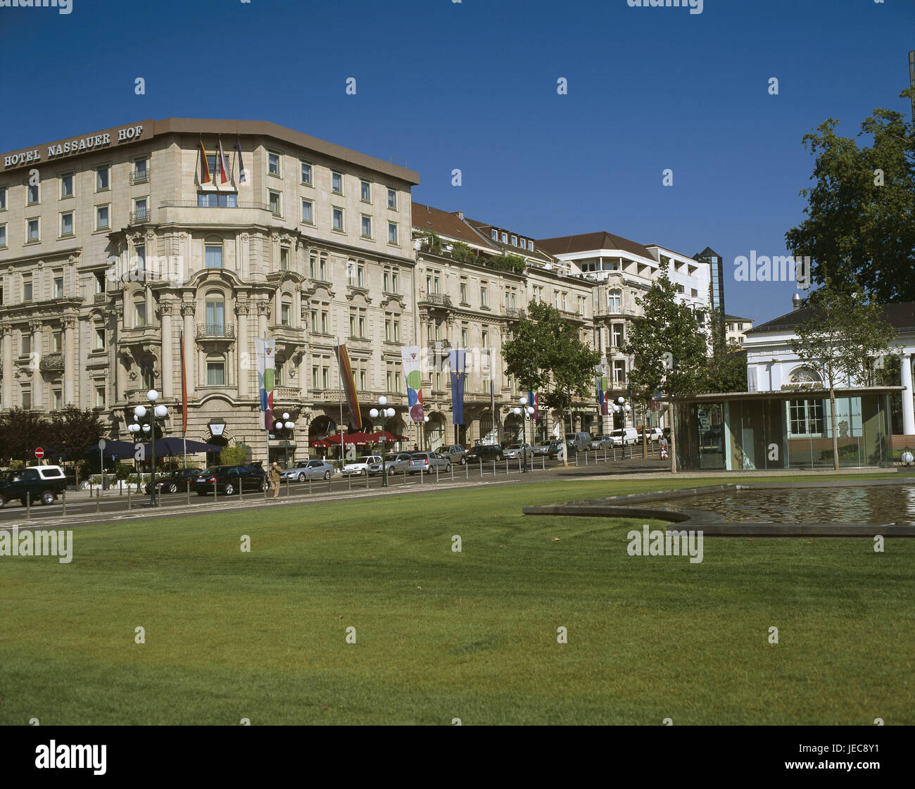Deutschland, Hessen, Wiesbaden, Wilhelmstraße, Schmarotzer Hotelhof, grüne Anlage, Stadt, Blick auf die Stadt, Straßenszene, Straße, Verkehr, Häuser, Gebäude, historisch, Fassaden, Architektur, Hotelgebäude, Eckhaus, Hotel Schmarotzer Gericht, Frühzeit, Person, Grünanlage, Wasser Becken, Laternen, Straßenlaternen, Fahnen, Boulevard, Boulevard, Ort von Interesse, Stockfoto
