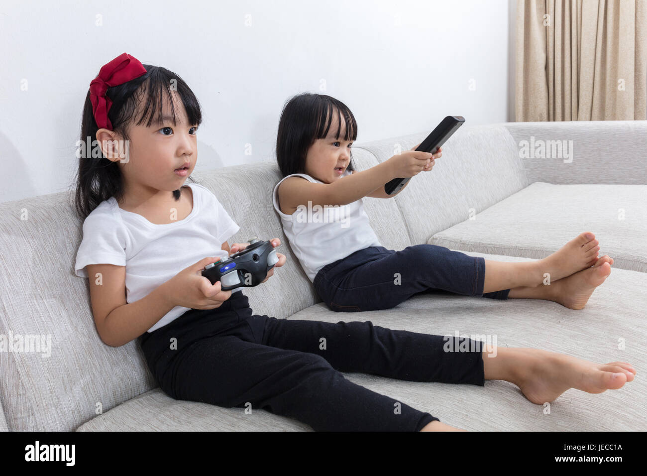 Asiatische chinesische kleinen Schwestern spielen TV auf dem Sofa im Wohnzimmer zu Hause. Stockfoto