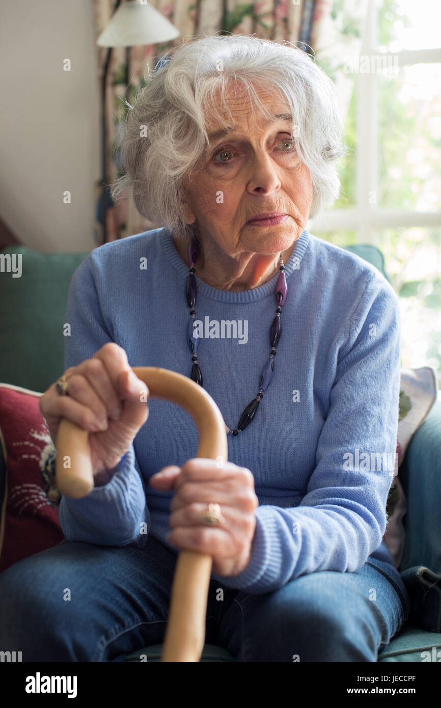 Traurige Senior Frau sitzen auf Stuhl halten Walking Cane Stockfoto