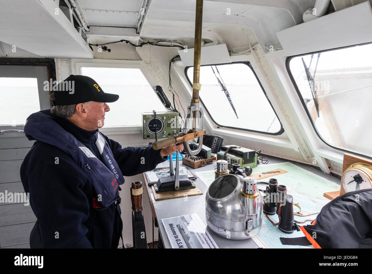 Älterer mann Pilotierung Boot, Innenraum des Schiffs Brücke, Mann in der Rettungsweste durch Fenster mit Blick auf das Meer. Von der Seite. Stockfoto