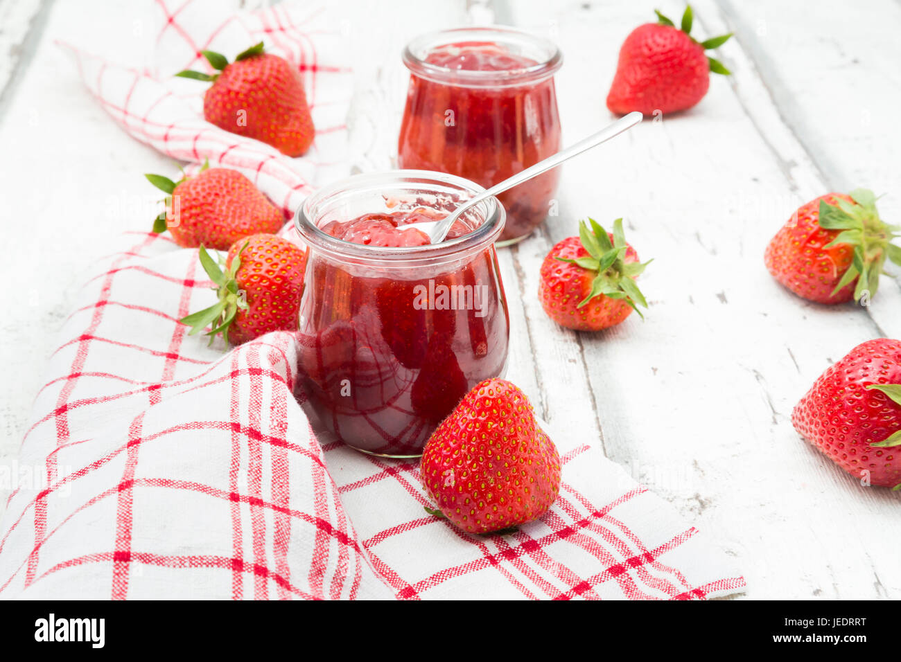 Glas hausgemachte Erdbeermarmelade, Küchentuch und Erdbeeren auf weißem Holz Stockfoto