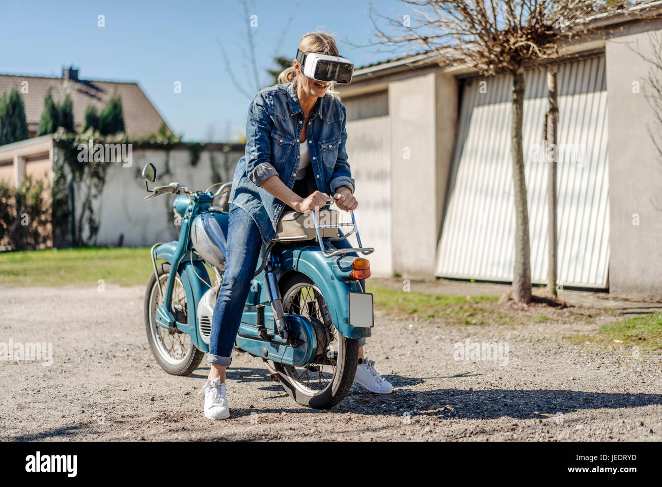 Frau sitzt hinten auf Vintage Motorrad mit VR-Brille Stockfoto