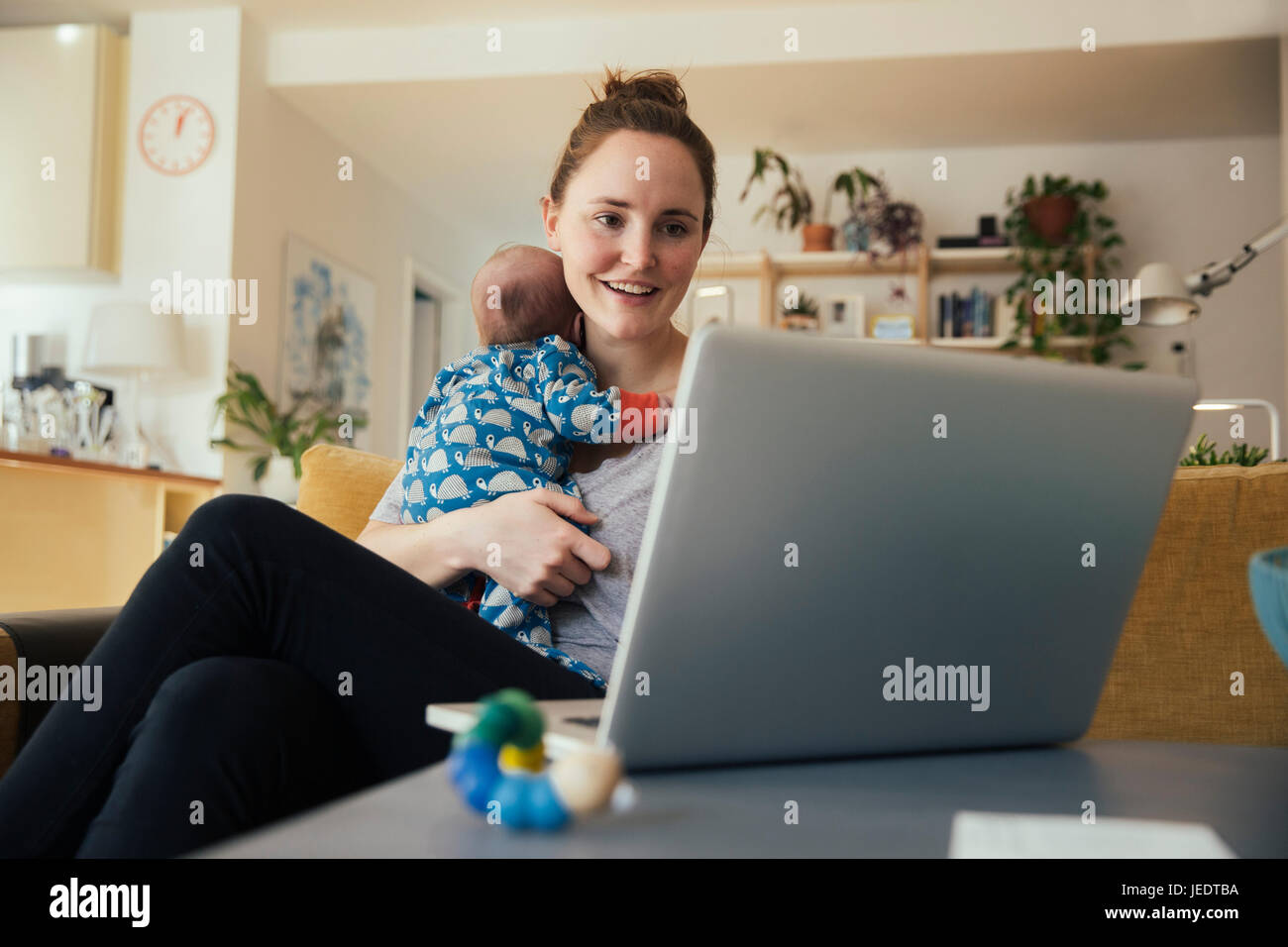 Mutter mit Laptop und halten ihr neugeborenes Baby zu Hause Stockfoto