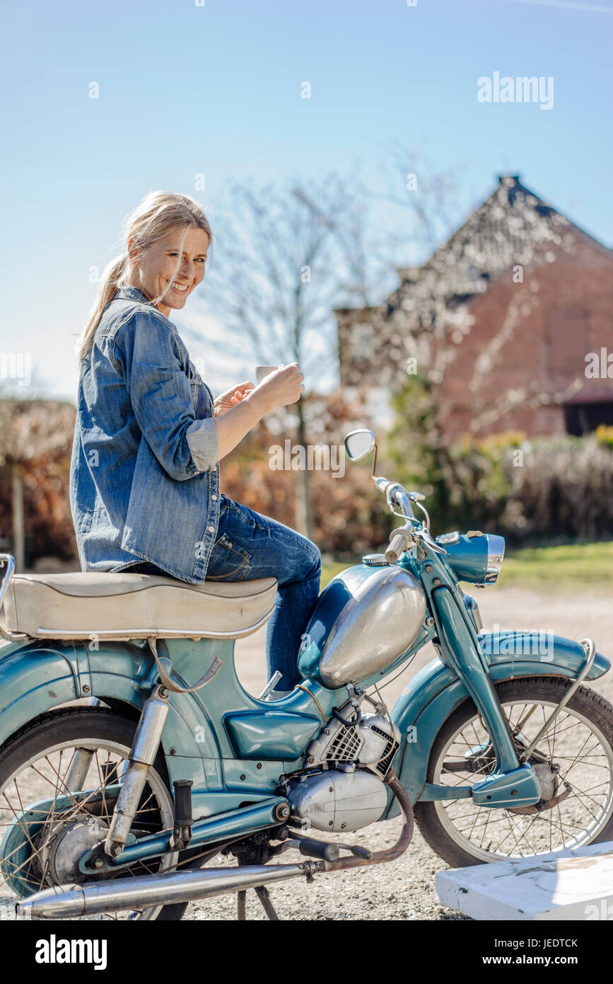 Lächelnde Frau auf Oldtimer Motorrad mit einer Kaffeepause Stockfoto