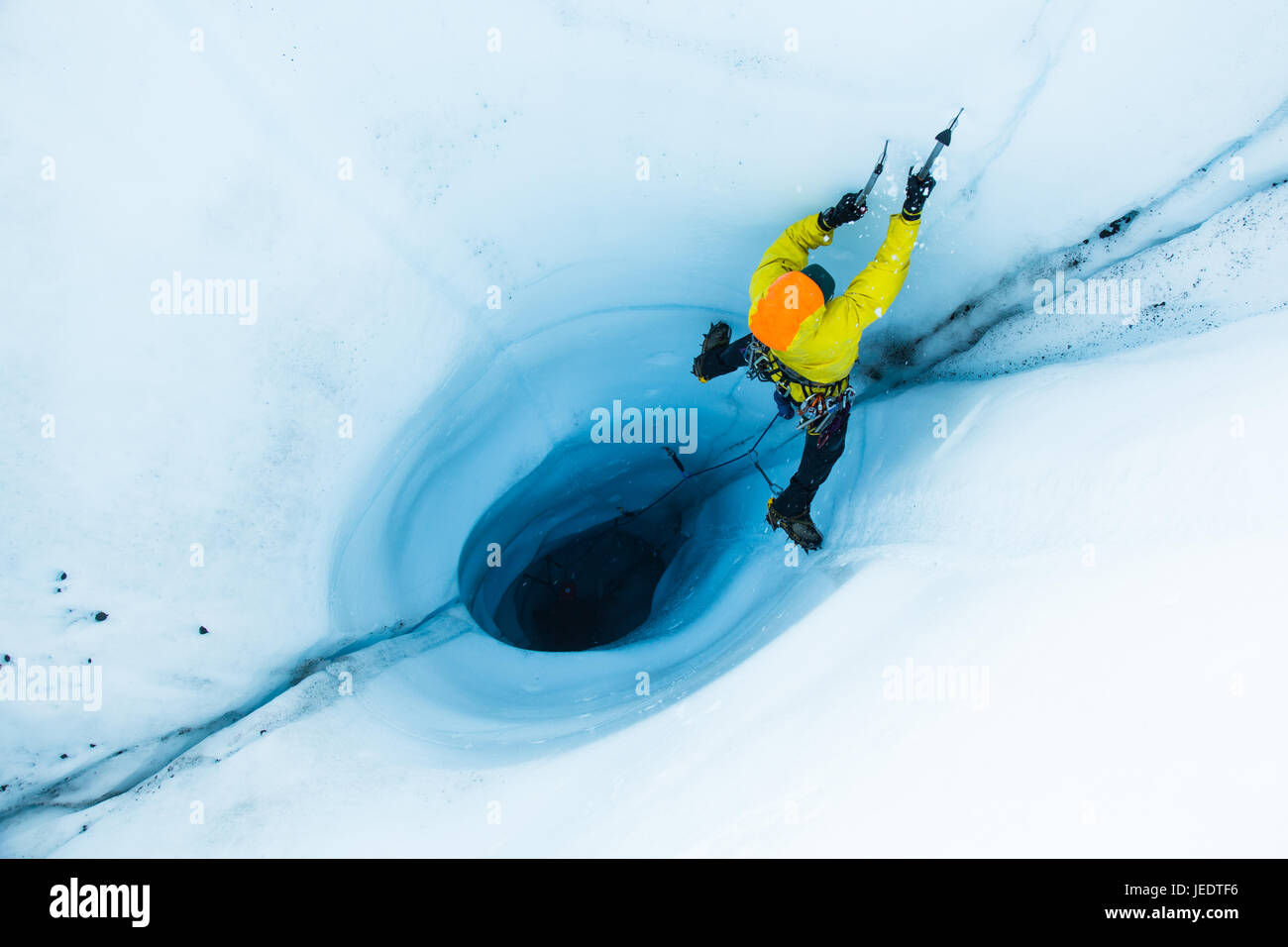 Ein Mann führen Eisklettern aus einen großen Moulin oder ein Loch in das Eis des Matanuska Gletscher in Alaska. Um den Aufstieg zu beginnen, seilte, er und seine sichernde Stockfoto