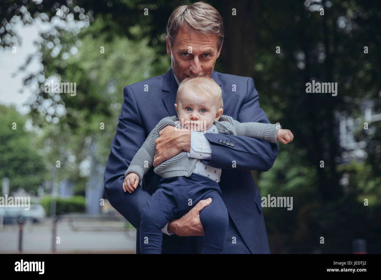 Porträt von reifer Geschäftsmann hält Baby Boy im freien Stockfoto