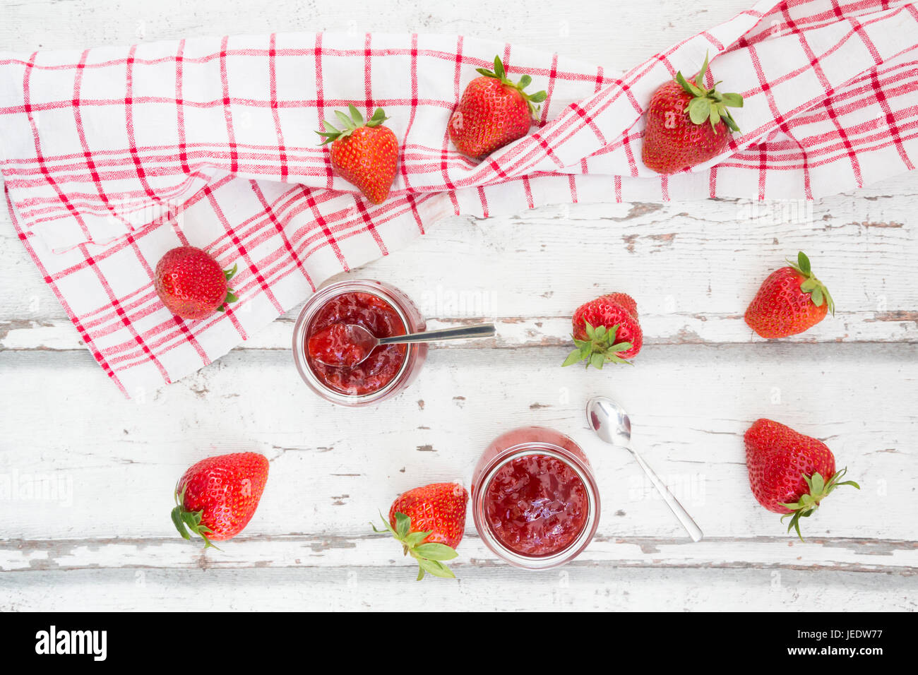 Zwei Gläser hausgemachte Erdbeermarmelade, Küchentuch und Erdbeeren auf weißem Holz Stockfoto