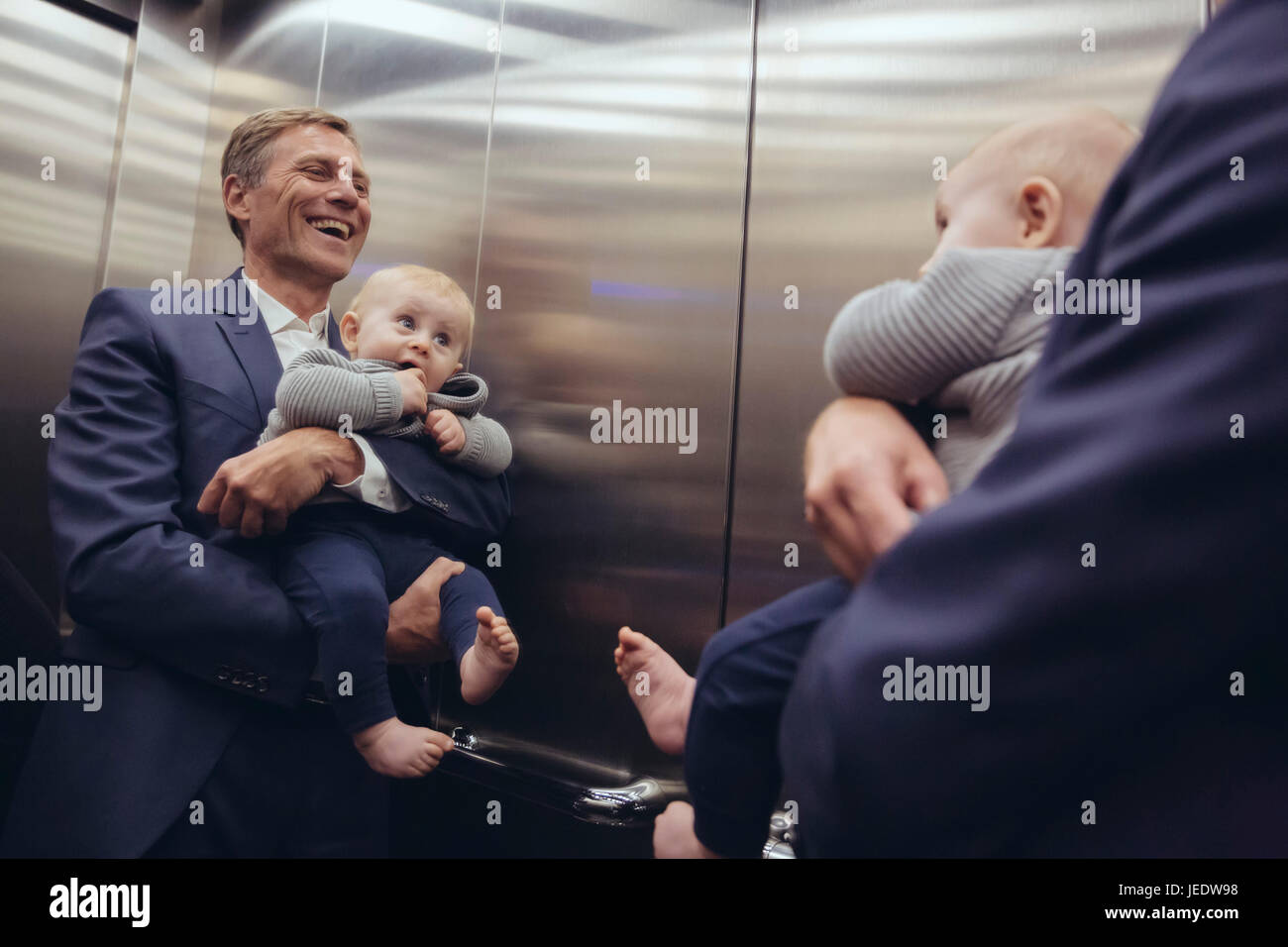 Glücklich reifer Geschäftsmann hält Baby Boy in Spiegel im Aufzug Stockfoto