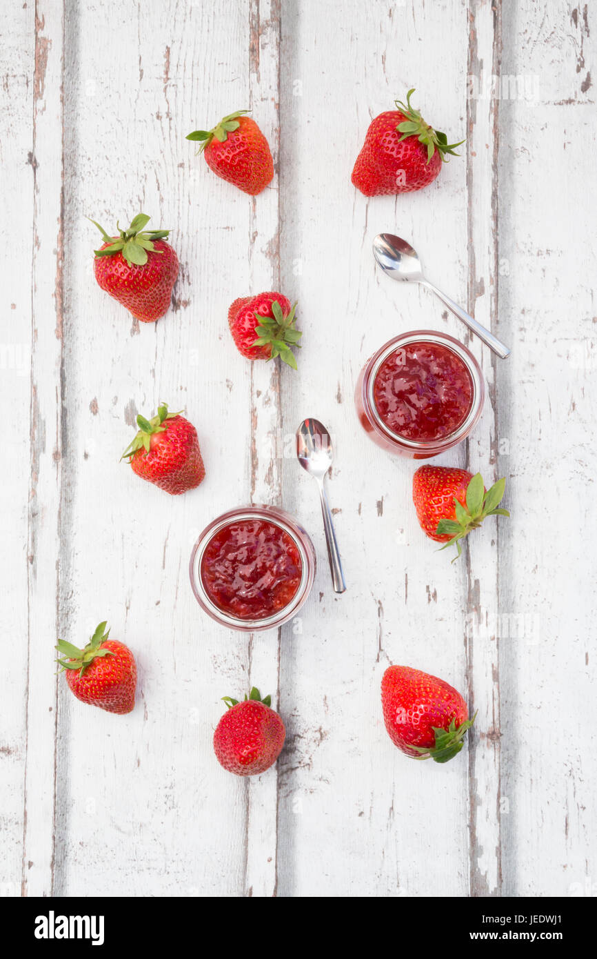 Zwei Gläser hausgemachte Erdbeermarmelade, Teelöffel und Erdbeeren auf weißem Holz Stockfoto