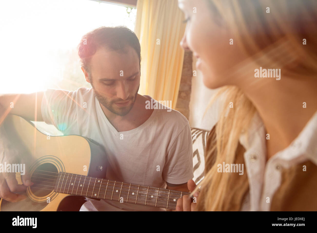 Mann spielt Gitarre zu Hause, während seine Freundin beobachtete ihn Stockfoto