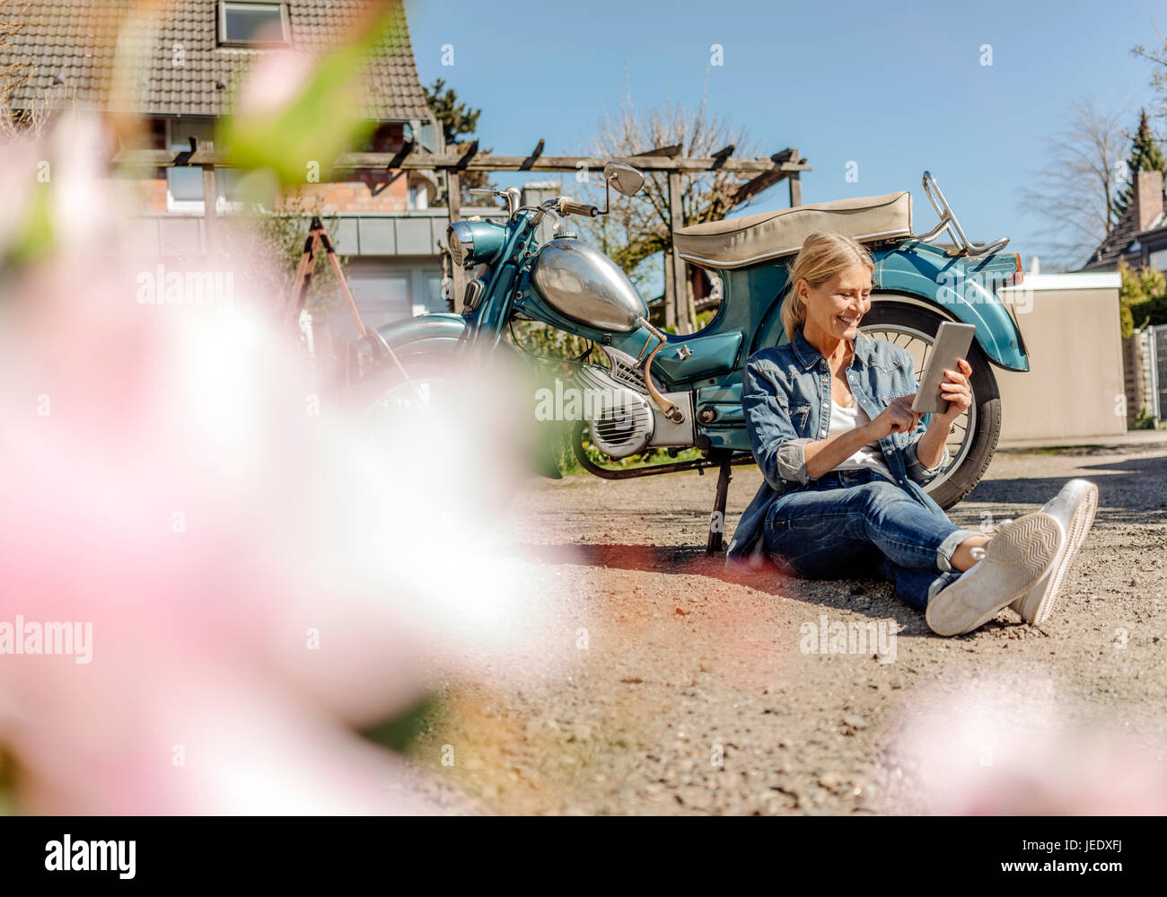 Lächelnde Frau sitzt am Oldtimer Motorrad mit tablet Stockfoto
