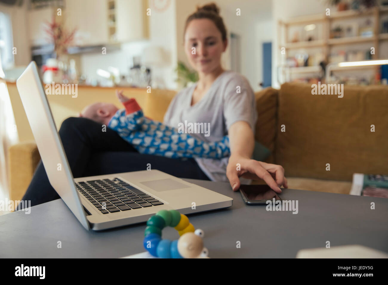 Mutter mit Neugeborenen zu Hause nehmen Handy aus Tabelle Stockfoto