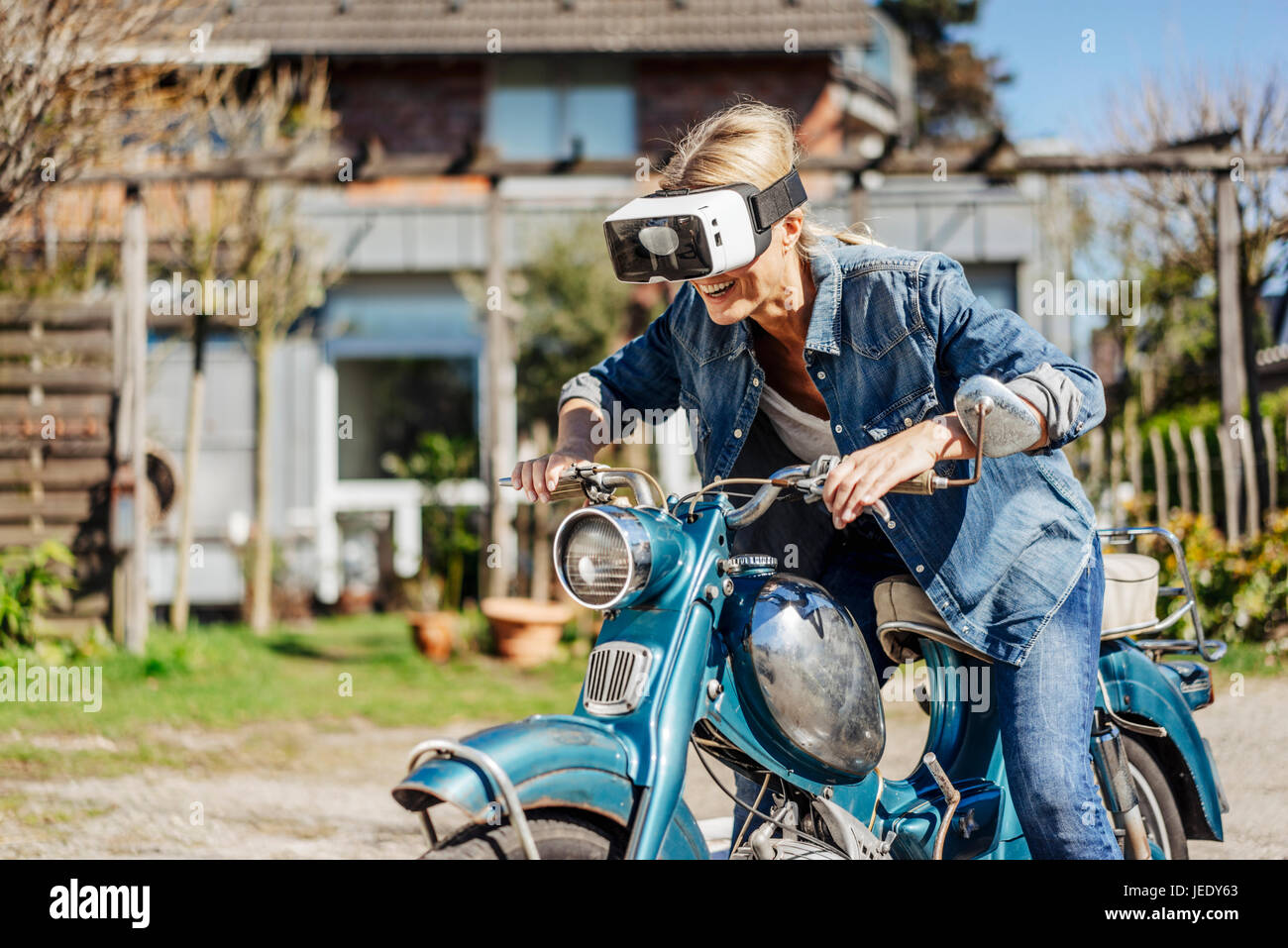 Glückliche Frau auf Oldtimer Motorrad mit VR-Brille Stockfoto