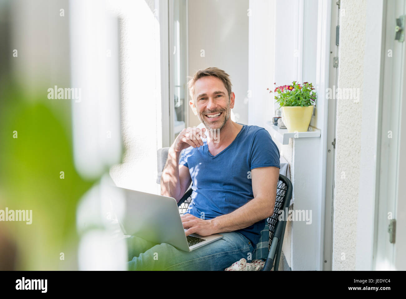 Porträt von lächelnden reifer Mann sitzen auf Balkon mit laptop Stockfoto