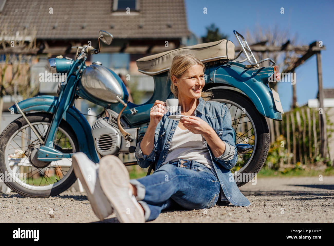 Lächelnde Frau sitzt am Oldtimer Motorrad mit einer Kaffeepause Stockfoto