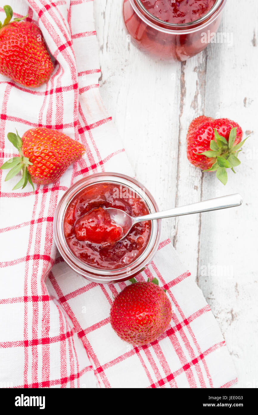 Glas hausgemachte Erdbeermarmelade, Küchentuch und Erdbeeren auf weißem Holz Stockfoto