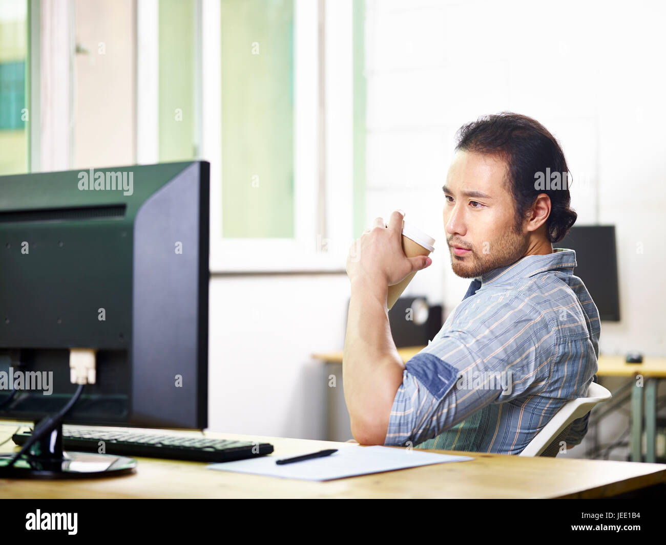 asiatische Geschäftsmann arbeiten im Büro hält eine Tasse Kaffee mit Blick auf Desktop-computer Stockfoto