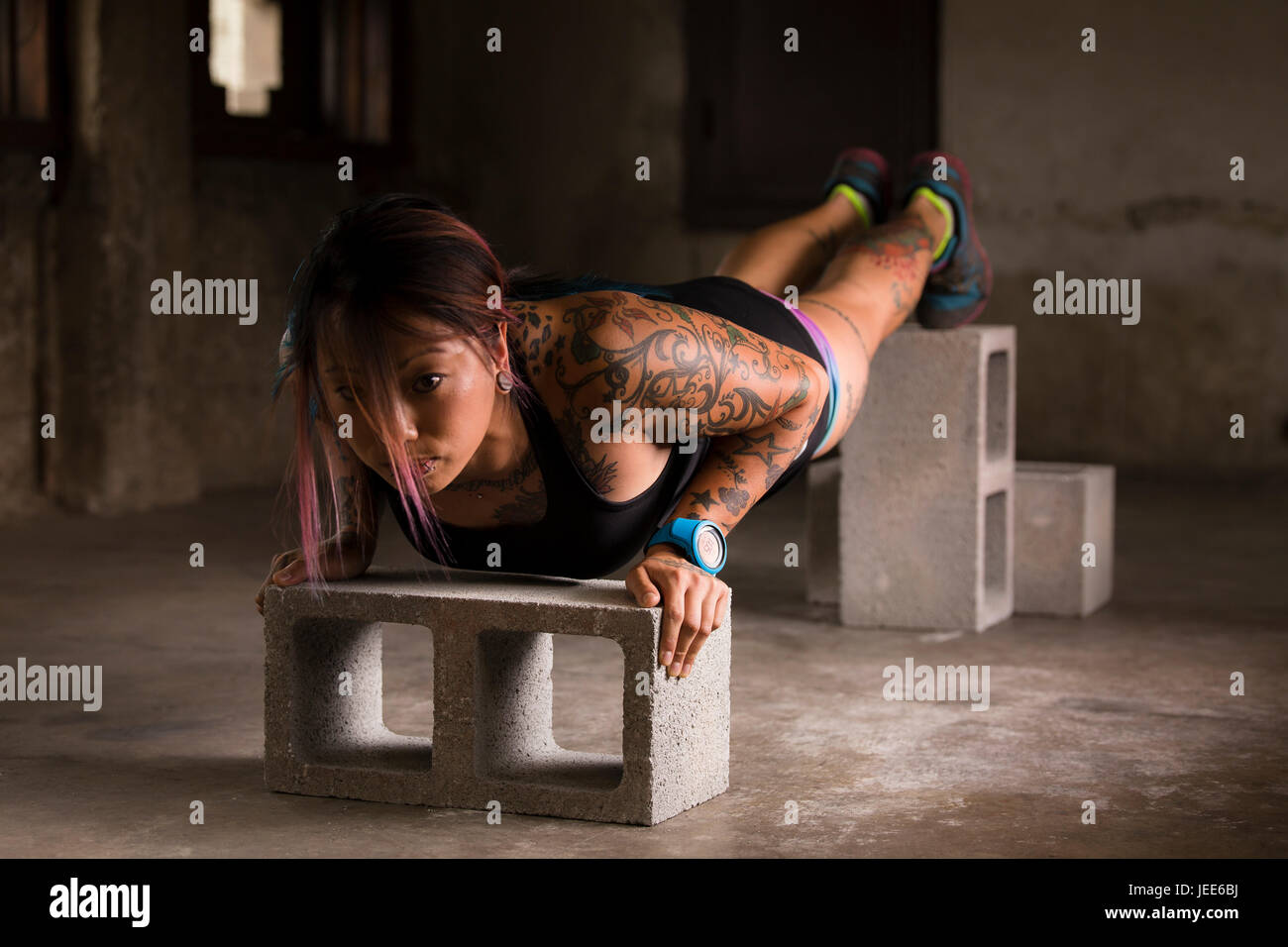 Sportliche junge Asiatin mit Tattoos Körper Gewicht Übungen in einem konkreten Lager mit Betonblöcken Stockfoto