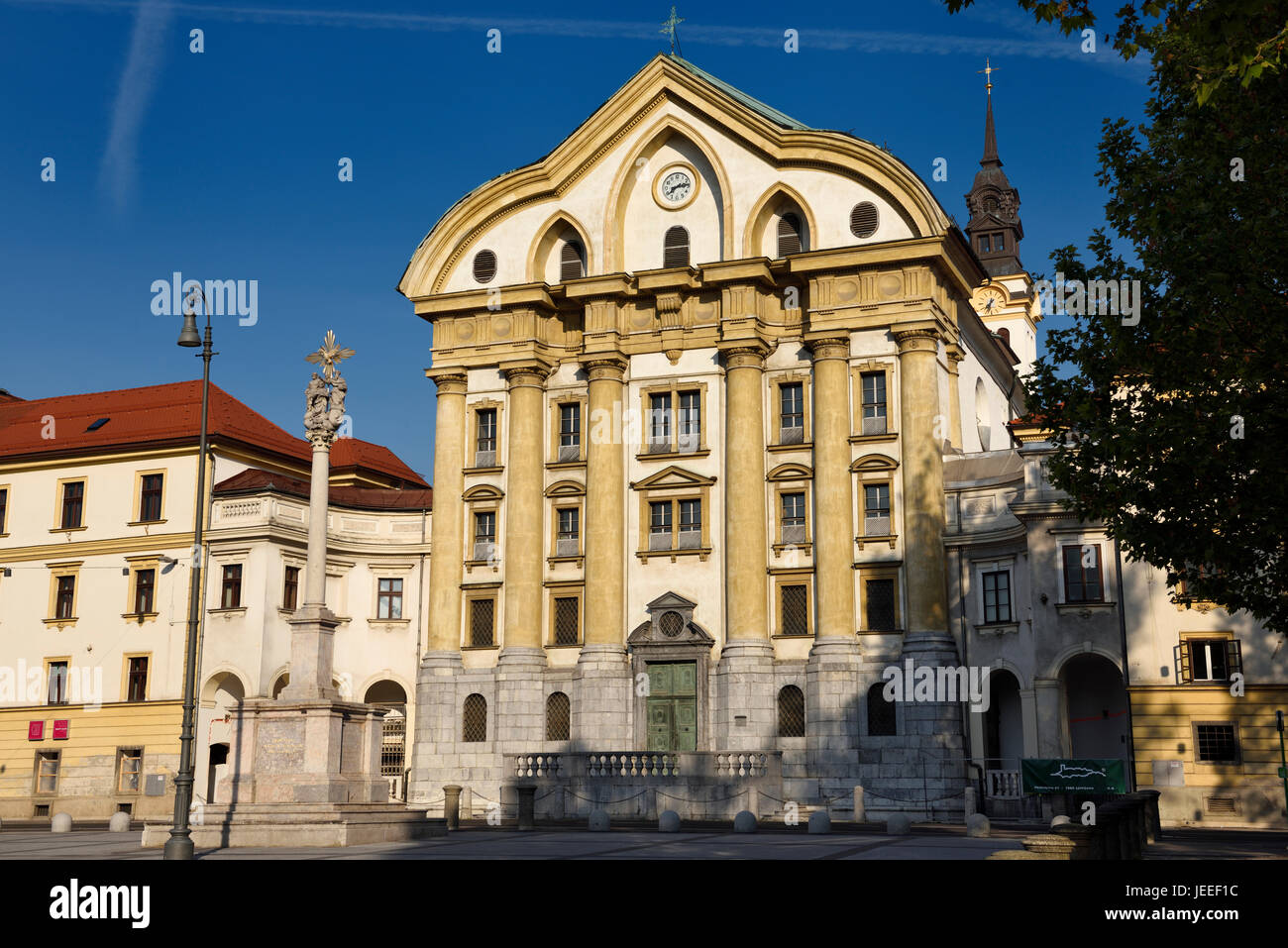 Sonnenschein auf die Ursulinen-Kirche der Heiligen Dreifaltigkeit mit Marmor-Statuen der Heiligen Dreifaltigkeit Spalte in Ljubljana Slowenien mit Uhr und der Glockenturm Stockfoto