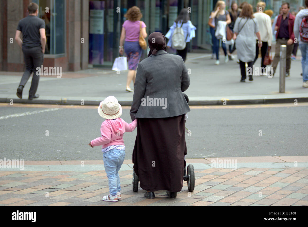 Asiatische Familie Flüchtling gekleidet Hijab Schal auf Straße im UK alltägliche Szene Mutter und Kind Stroh Hut Stockfoto