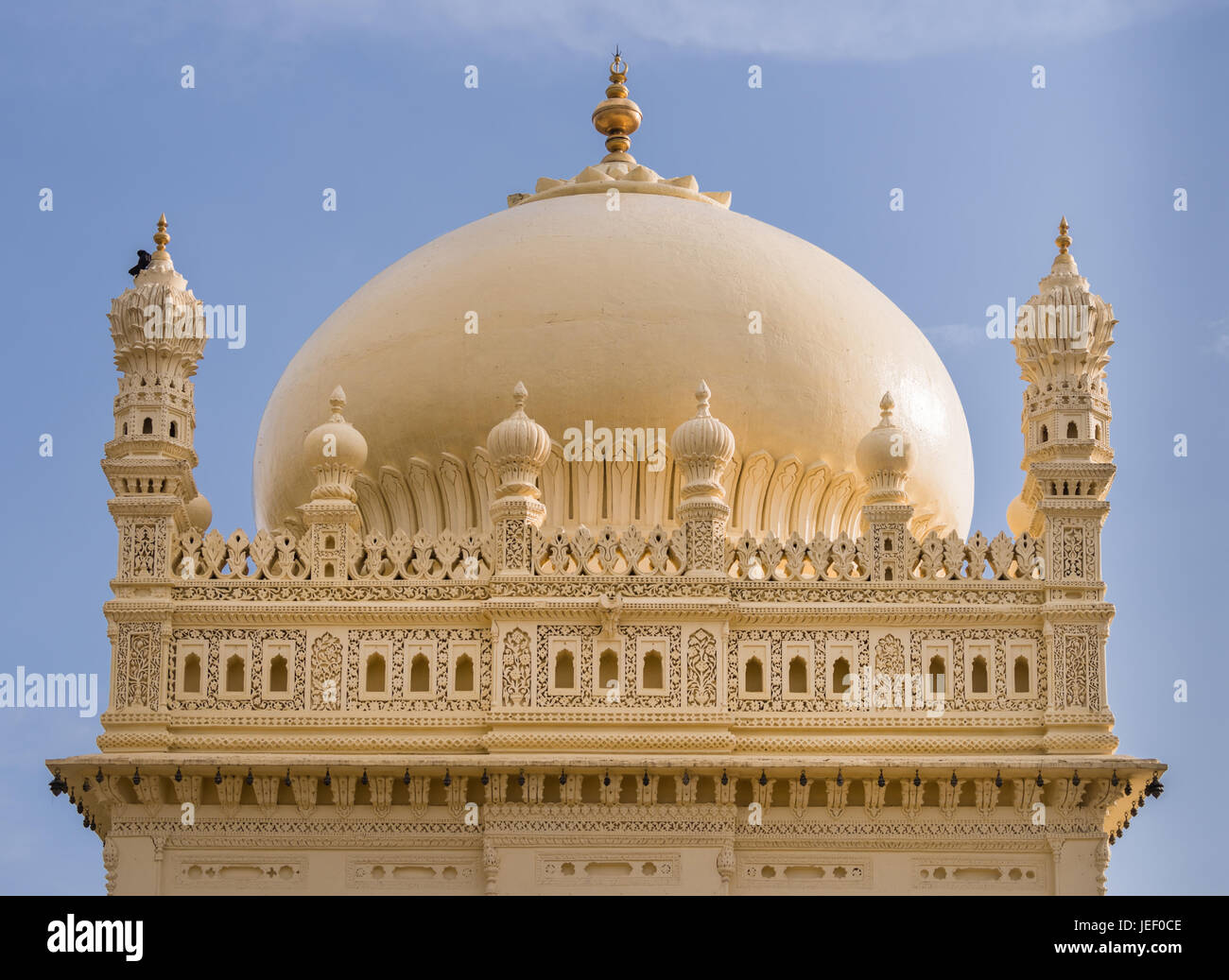 Mysore, Indien - 26. Oktober 2013: Obere Struktur und Kuppel der Creme gelb Tipu Sultan Mausoleum unter blauem Himmel. Goldene Kalasam an der Spitze. Ein schwarzer Vogel Stockfoto