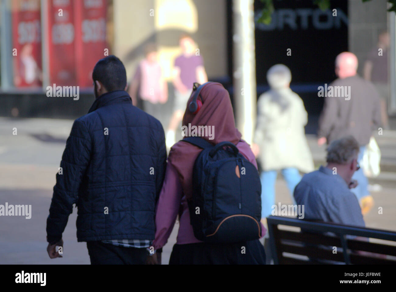 Asiatische Familie Flüchtling gekleidet Hijab Schal auf Straße in der UK alltägliche Szene junges Paar Mädchen Kopfhörer auf Schal Musikhören Stockfoto