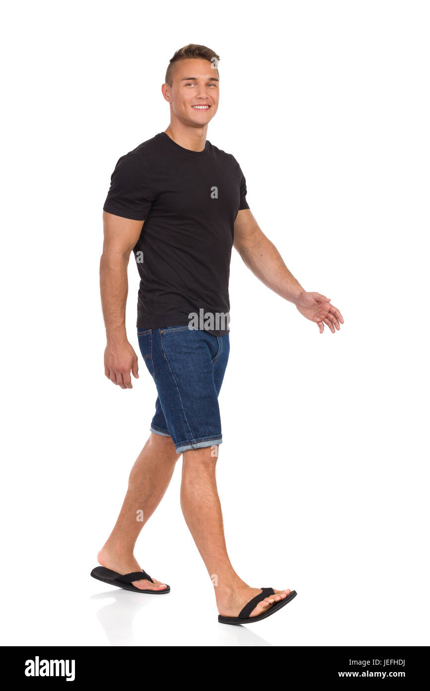 Junger Mann im schwarzen Hemd, Jeans-Shorts und schwarze Sandalen Wander- und Blick in die Kamera. Voller Länge Studio gedreht isoliert auf weiss. Stockfoto